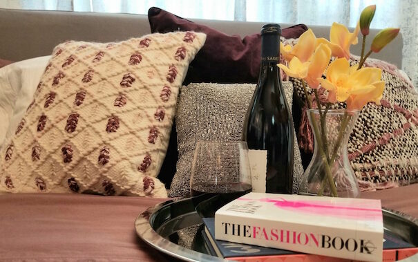 A tray with wine, flowers, and a book kept on a bed