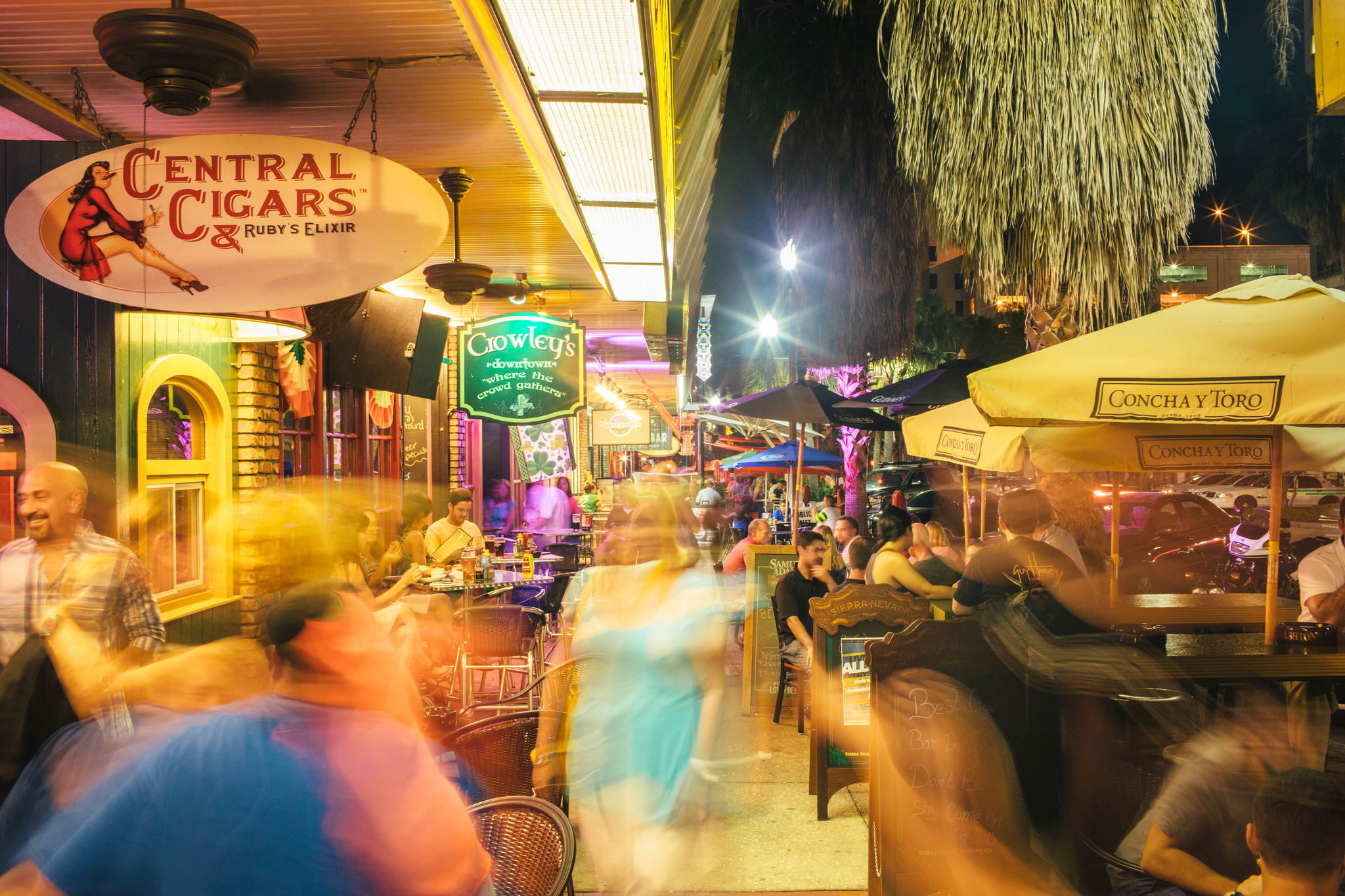 A busy street with people walking and sitting on chairs.
